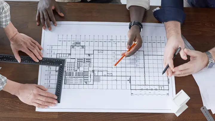 Several hands working around a floor plan on a wooden table